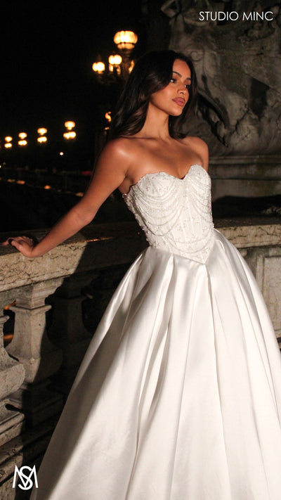 Woman in a white wedding dress with beaded bodice standing on a stone bridge in Paris at night.